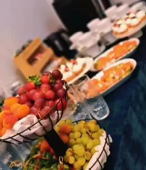Augļu un ogu vāzes ar vīnogām, zemenēm un aprikozēm uz bufetes galda